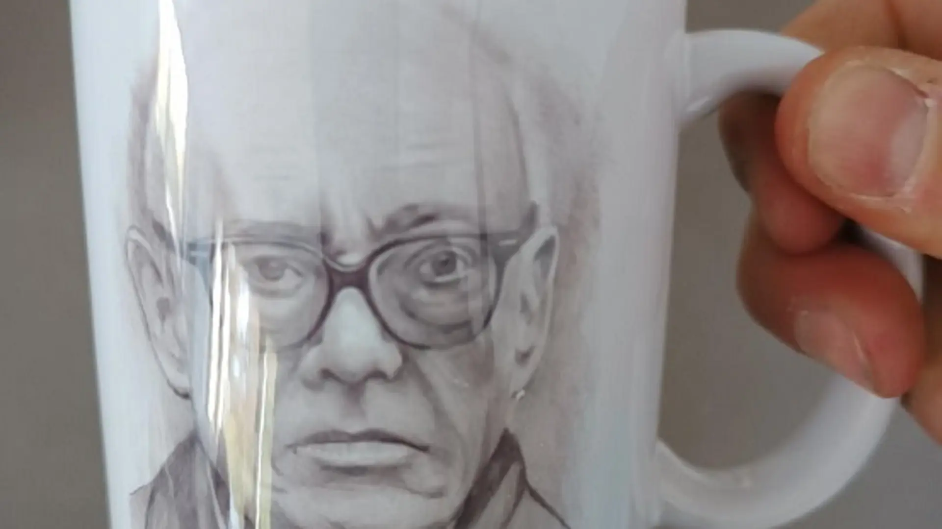 Nahaufnahme von einer Hand, die eine Tasse mit dem darauf gedruckten Porträt von Ernst Jandl, dem Schulpatron, hält.