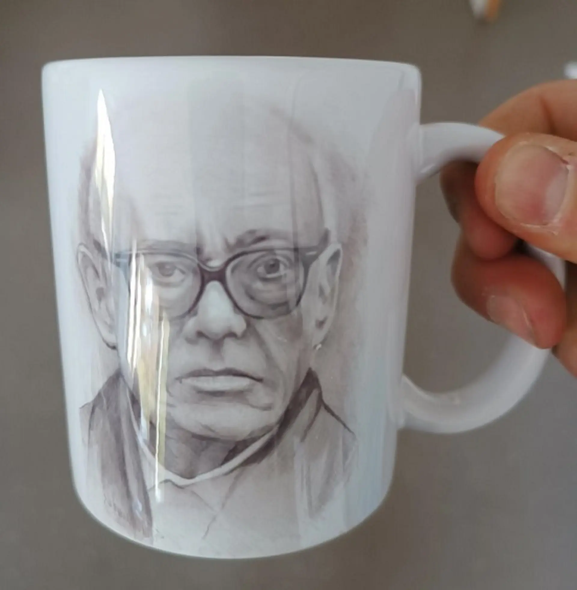Nahaufnahme von einer Hand, die eine Tasse mit dem darauf gedruckten Porträt von Ernst Jandl, dem Schulpatron, hält.