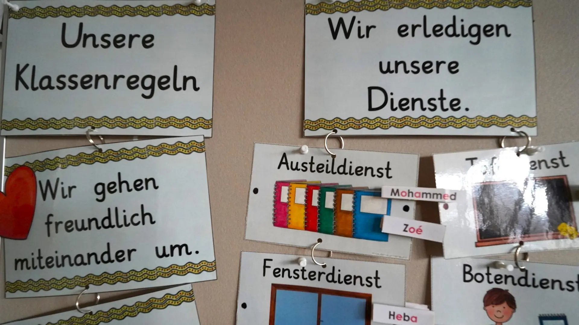 Eine Übersichtstafel in einem Klassenzimmer der LVR-Ernst-Jandl-Schule mit bebilderten Klassenregeln und einer Einteilung der verschiedenen Klassendienste für die Schüler*innen.